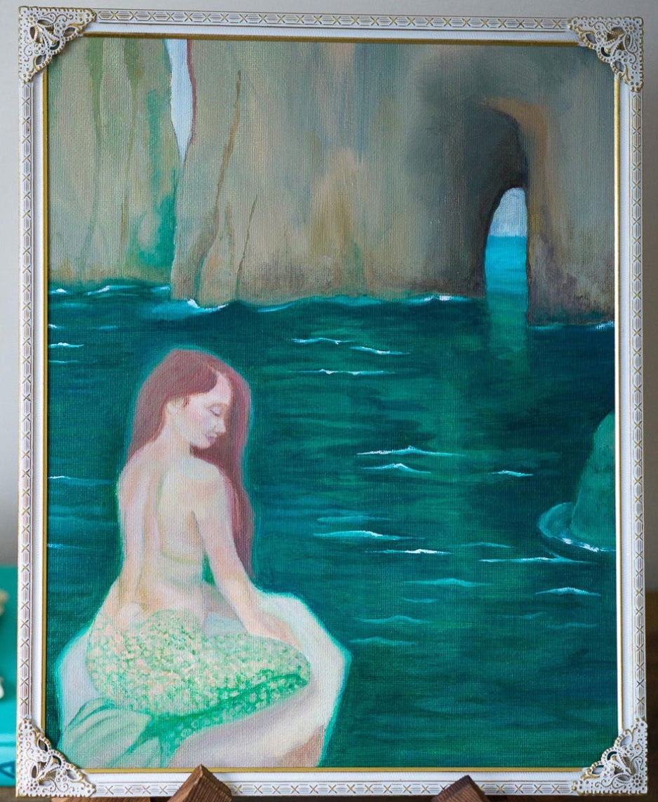 A framed painting of a mermaid in a sea cave